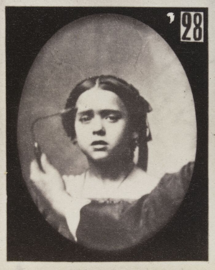 Black and white 19th century facial expressions experiment showing a young woman with a solemn, tense expression and wires attached.