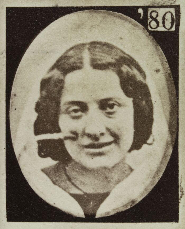 Sepia tone image from 19th century facial expressions experiment showing a woman with unusual facial distortion and a pipe.