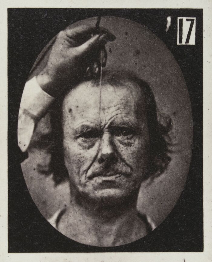 Black and white 19th century facial expressions experiment with a man holding a pendulum over his face.