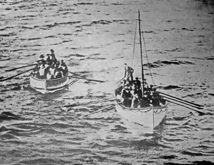 Two lifeboats filled with people rowing on calm water in a rare historical photo related to the Titanic.