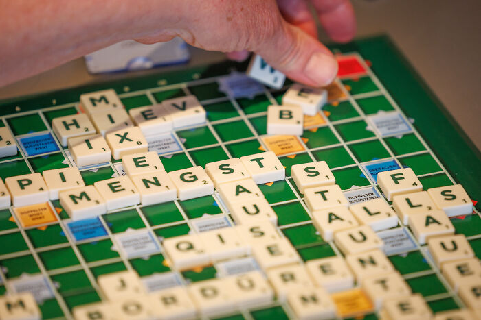 Hand placing letter tiles on a Scrabble board illustrating fear of long words and the world&rsquo;s cruelest phobia.