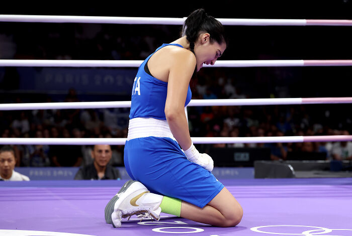 Female boxer kneeling in the ring, wearing blue gear, representing the boxer who refused to fight Imane Khelif amid harassment claims.