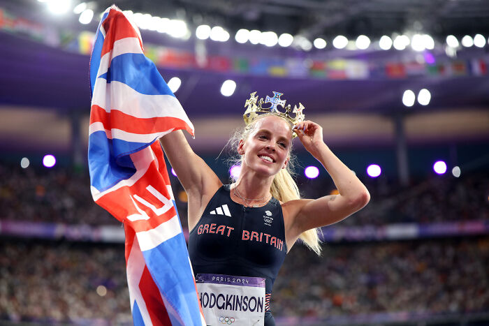 Olympic gold medalist Keely Hodgkinson celebrating victory, holding British flag and wearing a gold crown at Paris 2024 Games.