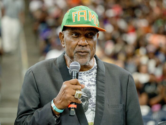 College band announcer speaking into microphone at event, linked to bodyshaming plus-size dancers and backlash apology.