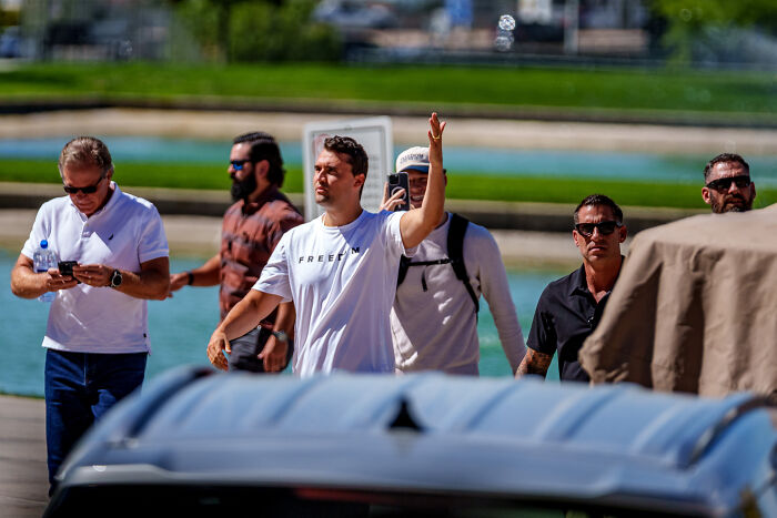 Group of men outdoors with one raising a hand, unrelated to Charlie Kirk sniper&rsquo;s rooftop nest eerie photos perspective.