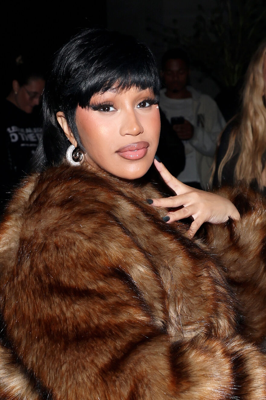 Cardi B wearing a brown fur coat and hoop earrings, posing confidently, highlighting her rising net worth and music influence.