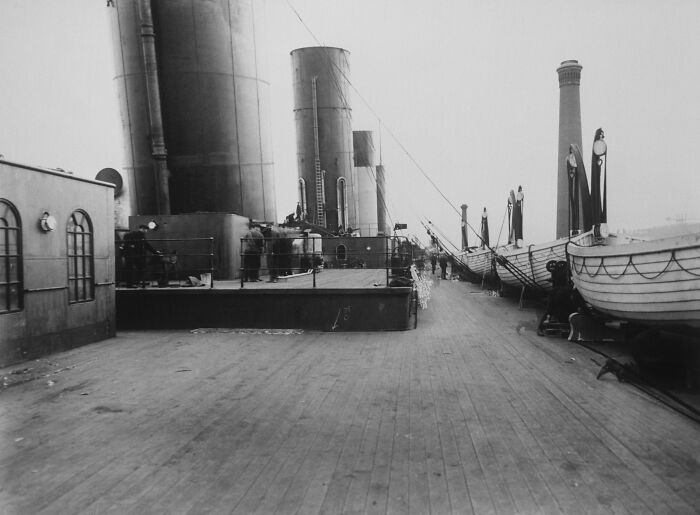 Rare historical photo of the Titanic deck showing lifeboats and smokestacks on the ship's wooden surface in black and white.