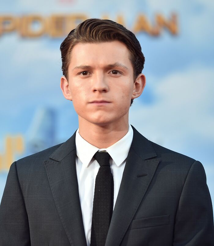 Tom Holland in a black suit and tie at a Spider-Man event, related to a head injury after a stunt accident. Tom Holland in a black suit and tie at a Spider-Man event, related to a head injury after a stunt accident.