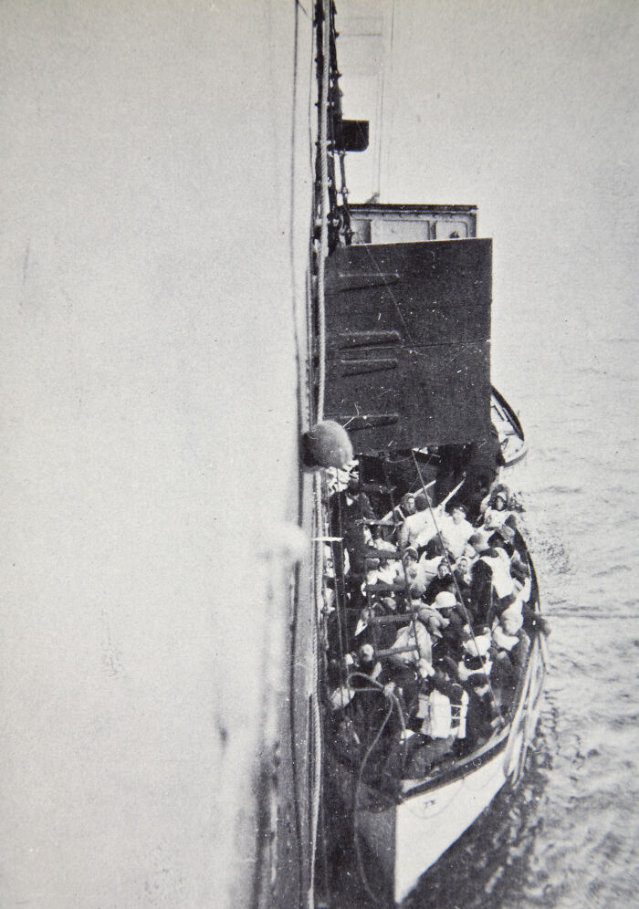 Black and white rare historical Titanic photo showing lifeboat crowded with passengers alongside the ship in the water.