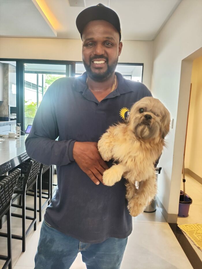 Pool attendant holding a small blind dog indoors, smiling after a heart-stopping rescue from drowning. Pool attendant holding a small blind dog indoors, smiling after a heart-stopping rescue from drowning.