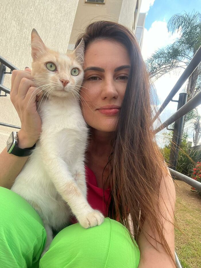 Woman with long hair holding a stray cat outdoors, showcasing a tiny condo for three stray cats project.