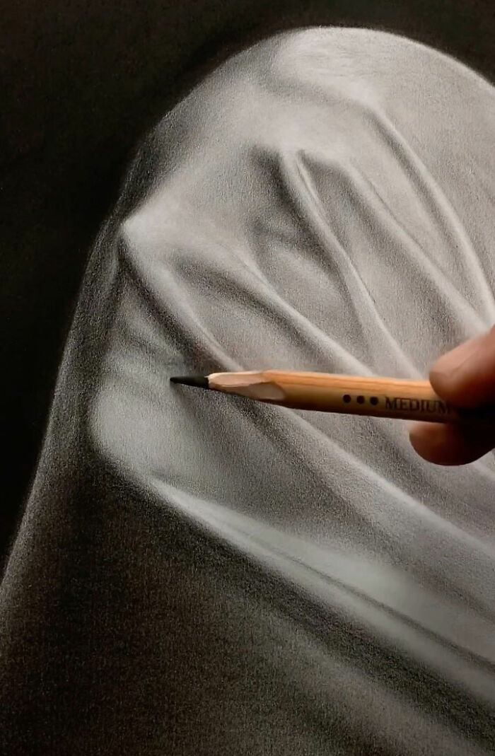 Close-up of a pencil creating an incredible pencil portrait showing detailed shading and texture of fabric folds.