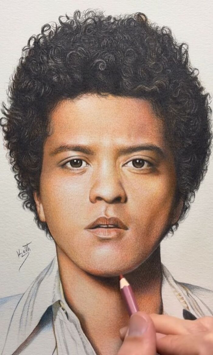 Hyper-realistic pencil portrait in progress showing detailed facial features and curly hair with an artist's hand adding color.