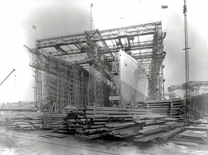 Rare historical photo of the Titanic under construction, showing scaffolding and steel beams at the shipyard.