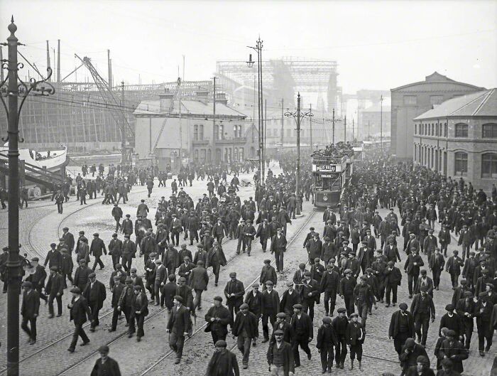 Crowd of workers walking near construction site of Titanic shipyard in rare historical photo from early 1900s.