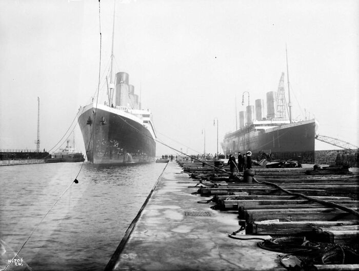 Two large ships docked at a harbor with workers on the pier in a rare historical photo of the Titanic.