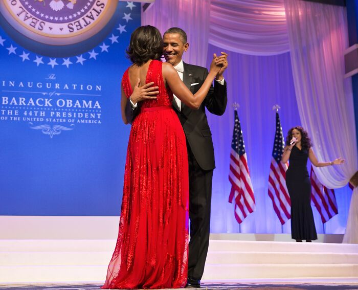 Barack Obama and Michelle Obama dancing at a formal event with American flags and a singer in the background. Barack Obama and Michelle Obama dancing at a formal event with American flags and a singer in the background.