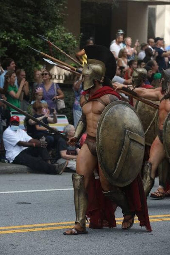 Reenactors dressed as ancient warriors with shields and spears parading, showcasing real life more interesting and bizarre than fiction.