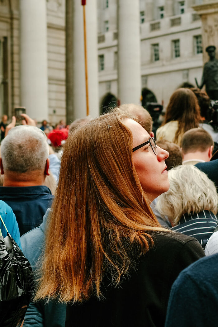 Woman with glasses standing in a crowd in London, capturing the atmosphere after the Queen’s passing during a public gathering.
