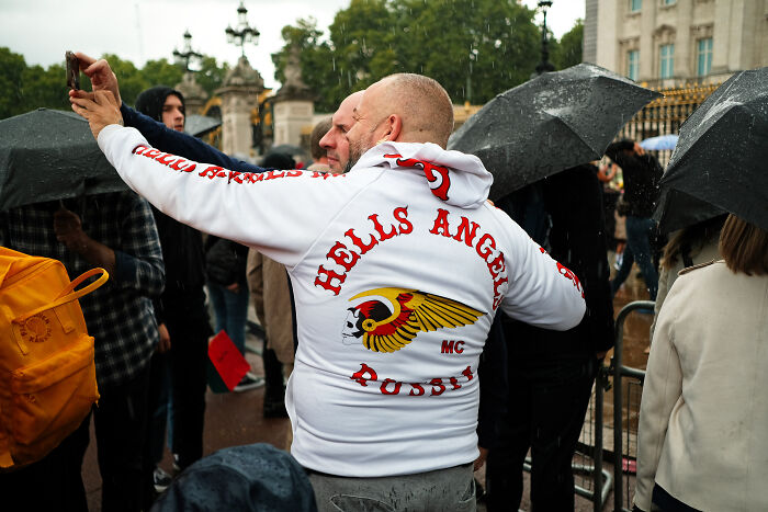 Crowd in London capturing the atmosphere with umbrellas and rain after the Queen’s passing outside a historic building.