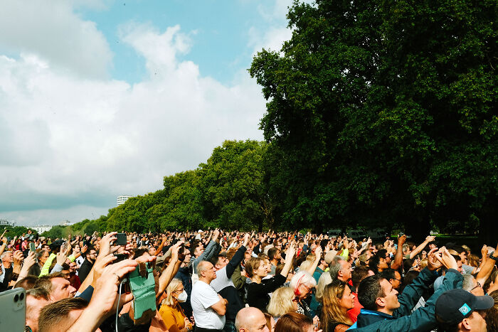 Crowd gathered in London, capturing the atmosphere with phones and cameras after the Queen’s passing during a bright daytime event.