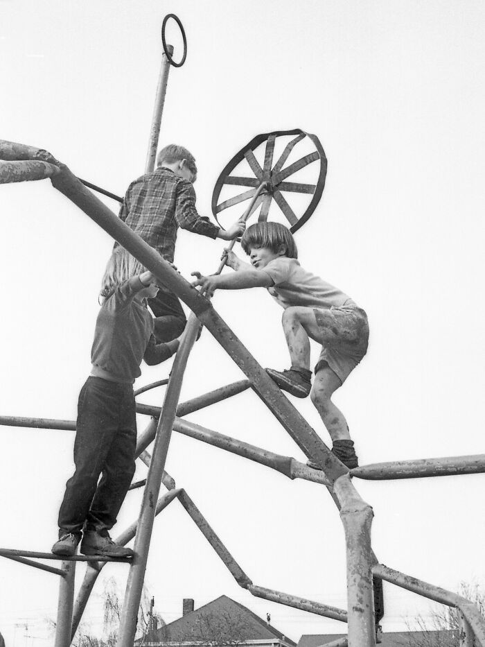 Three kids climbing on risky vintage playground equipment made of metal bars and a large wheel, showing historic playground safety.