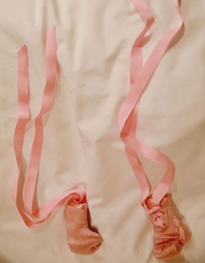 Pink baby boxing gloves with long ribbons placed on a light fabric background symbolizing Rihanna fans urging name change.