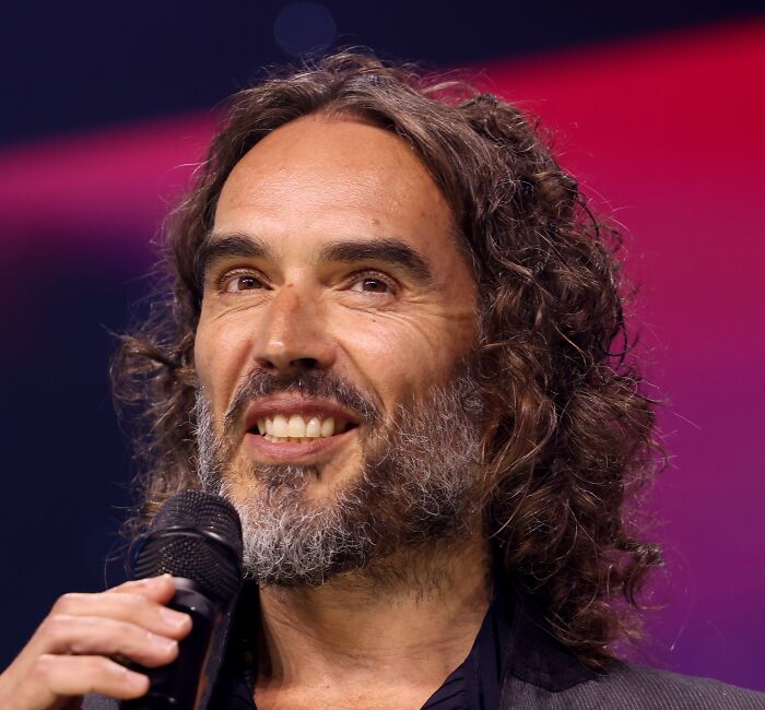 Russell Brand speaking into a microphone on stage, discussing the next big thing that totally flopped.