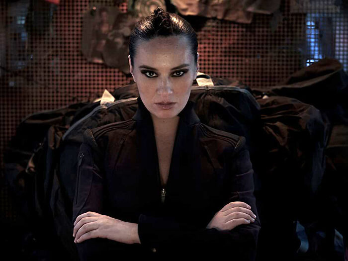 Female character in a dark outfit with crossed arms, portraying a well-written role that breaks stereotypes in movies.