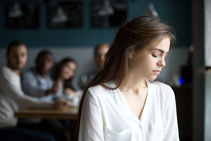 A young woman looking down with sadness while her family sits blurred in the background, symbolizing unwanted siblings adoption.