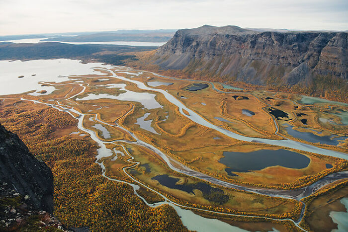 Vast autumn landscape in the far north with winding rivers, golden foliage, and rugged mountains under a clear sky.