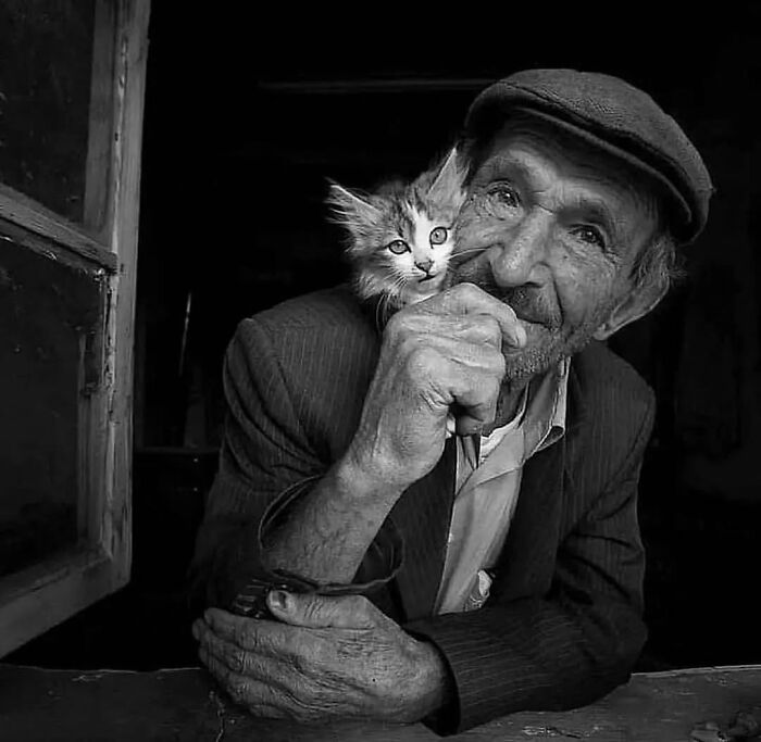 Elderly man with a cat on his shoulder in a powerful street photo capturing the beauty and wisdom of old age.
