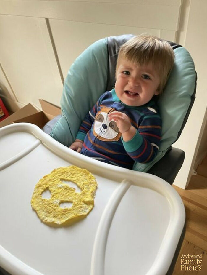 Toddler in a high chair reacting to a funny face-shaped egg made by funny parents creating amusing family moments.