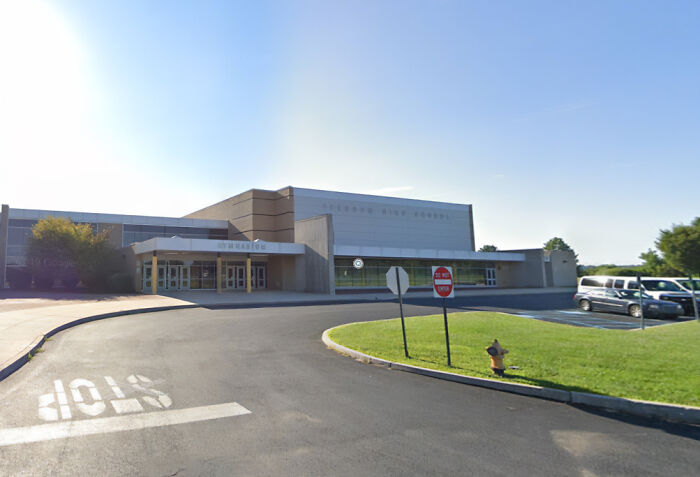 Suburban high school building exterior with parking lot and traffic signs, relating to viral TikTok trend injuries.