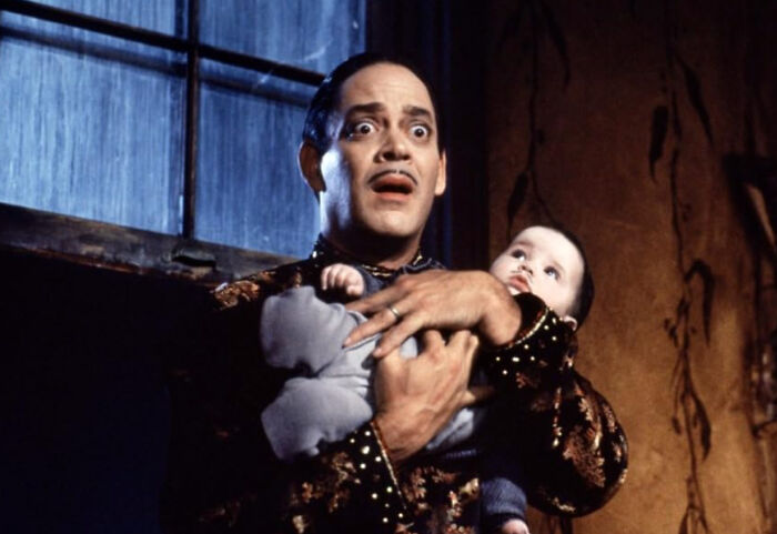 Man with shocked expression holding baby in dark room, evoking creepy stories perfect to tell in the dark woods.