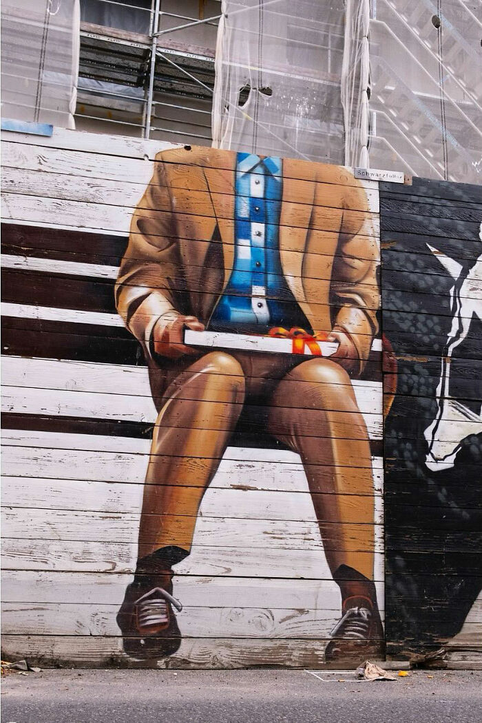 Mural of a headless man in a brown suit holding a gift box, showcasing entertaining street photographs timing.