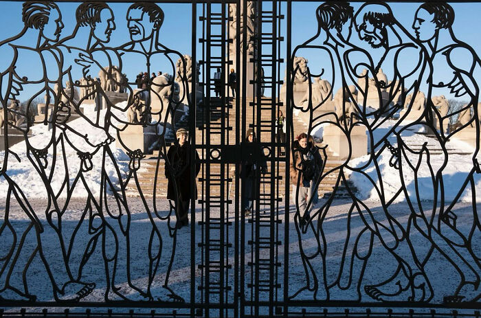Artistic metal gate with human and animal figures, framing pedestrians in a snowy street photograph highlighting perfect timing.