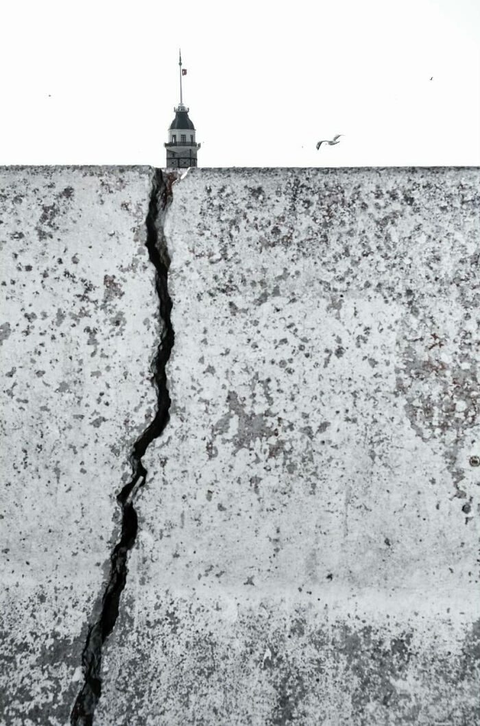 C*****d concrete wall with bird flying and a tower peeked over, an entertaining street photograph showing perfect timing.