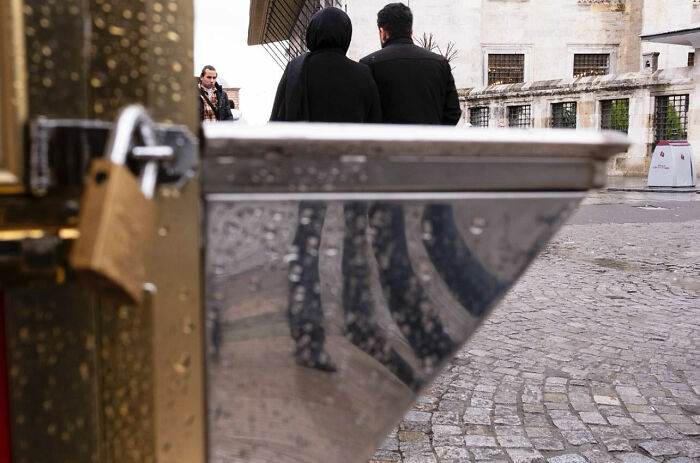 Couple walking on cobblestone street with water droplets reflecting their legs in an entertaining street photograph.