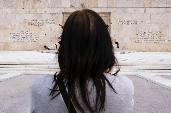 Person with long dark hair watching a precise moment of a guard performing in entertaining street photographs showcasing timing.