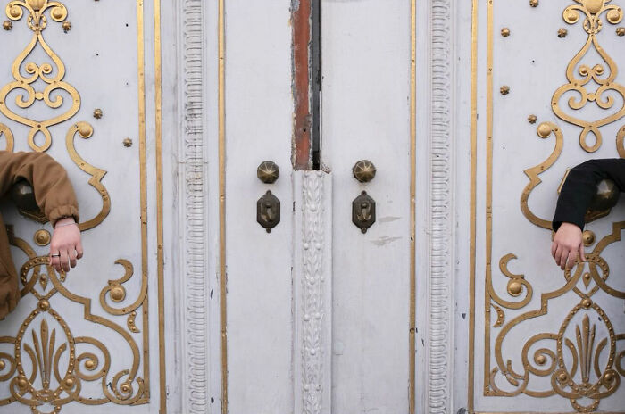 Two people with arms stretched through ornate golden street doors, capturing perfect timing in street photography.