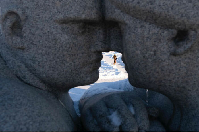 Close-up of two stone statues facing each other with a person walking in the snowy background, showcasing perfect timing in street photography.