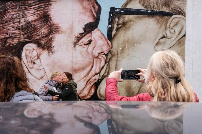 Couple kissing in front of a mural while another person captures the perfect timing street photograph.