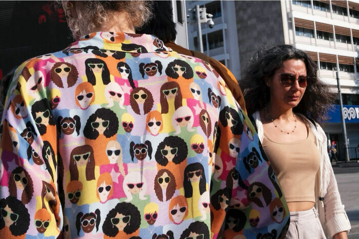 Street photograph capturing a colorful shirt with multiple faces and a woman walking in an urban setting showcasing timing.