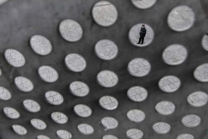 Man standing on a paved street captured through holes in a metal sheet in an entertaining street photograph showing perfect timing.