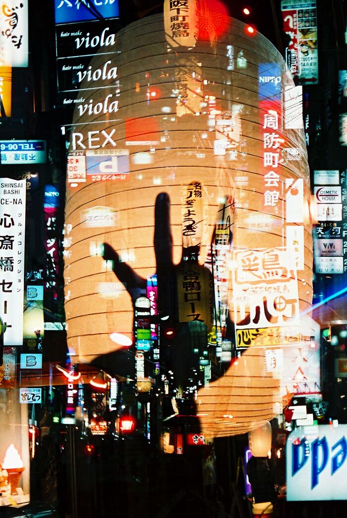 Analog photo with colorful urban night scene and a large lantern casting a hand shadow in Tokyo streets.