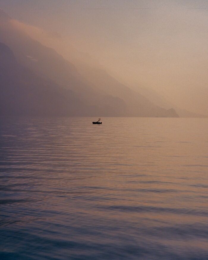 Small boat on calm water with misty mountains in the background in a serene analog photo.