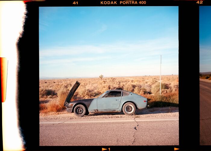 Analog photo of a vintage car with its hood open on a desert road, showcasing film photography quality.
