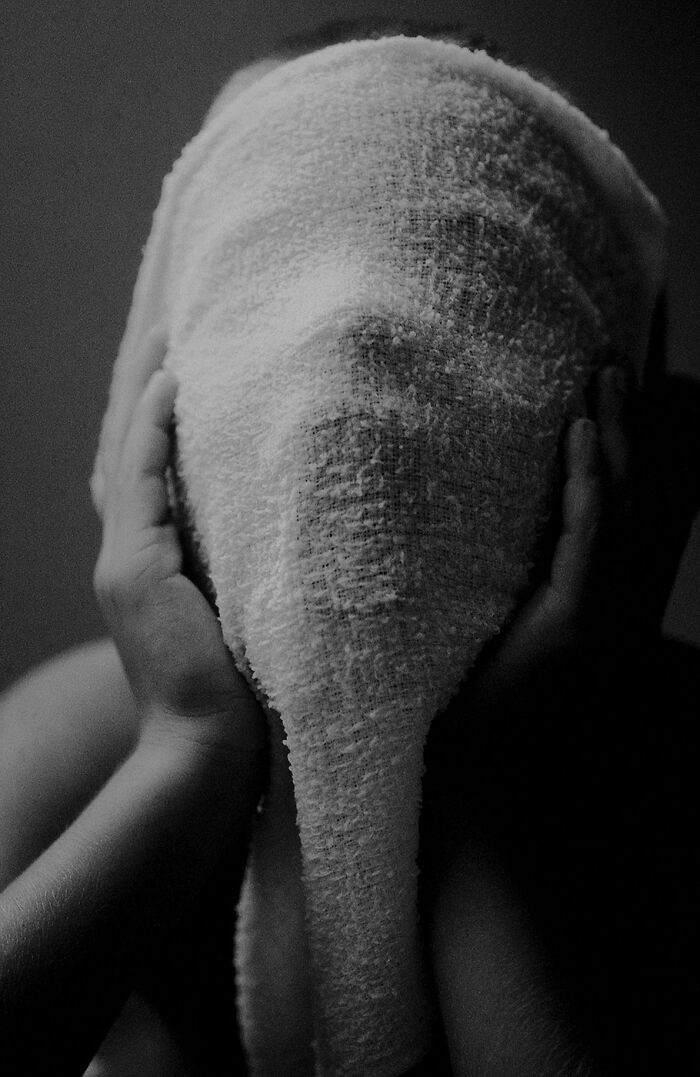Black and white minimalism photo of person covering face with textured fabric, hands holding fabric edges softly.