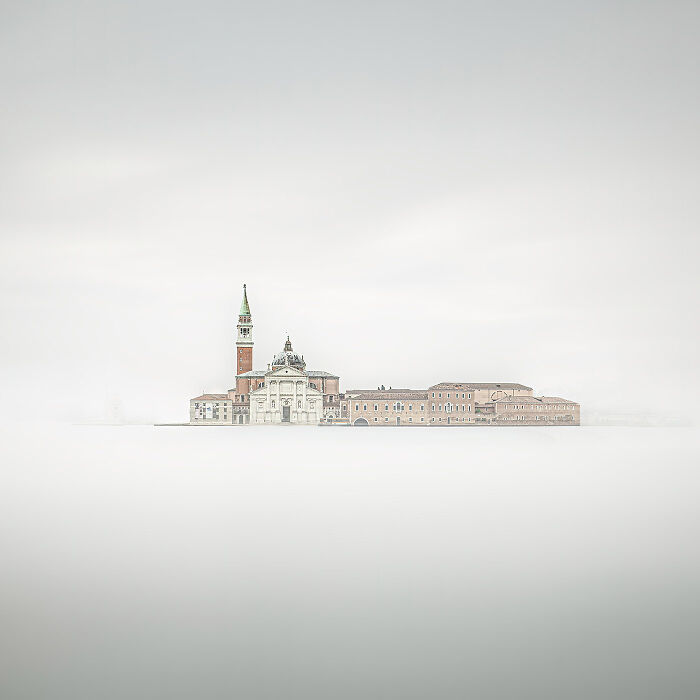 Minimalist photo of a historic building with a tall tower surrounded by soft, muted tones and empty space.